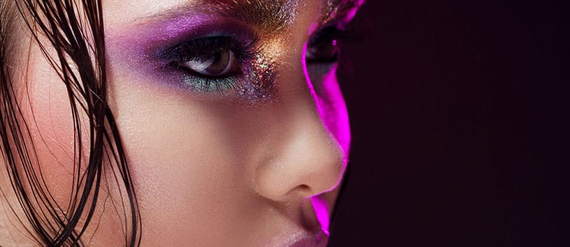 Close-up image of a woman with bright eye makeup and skin care.
