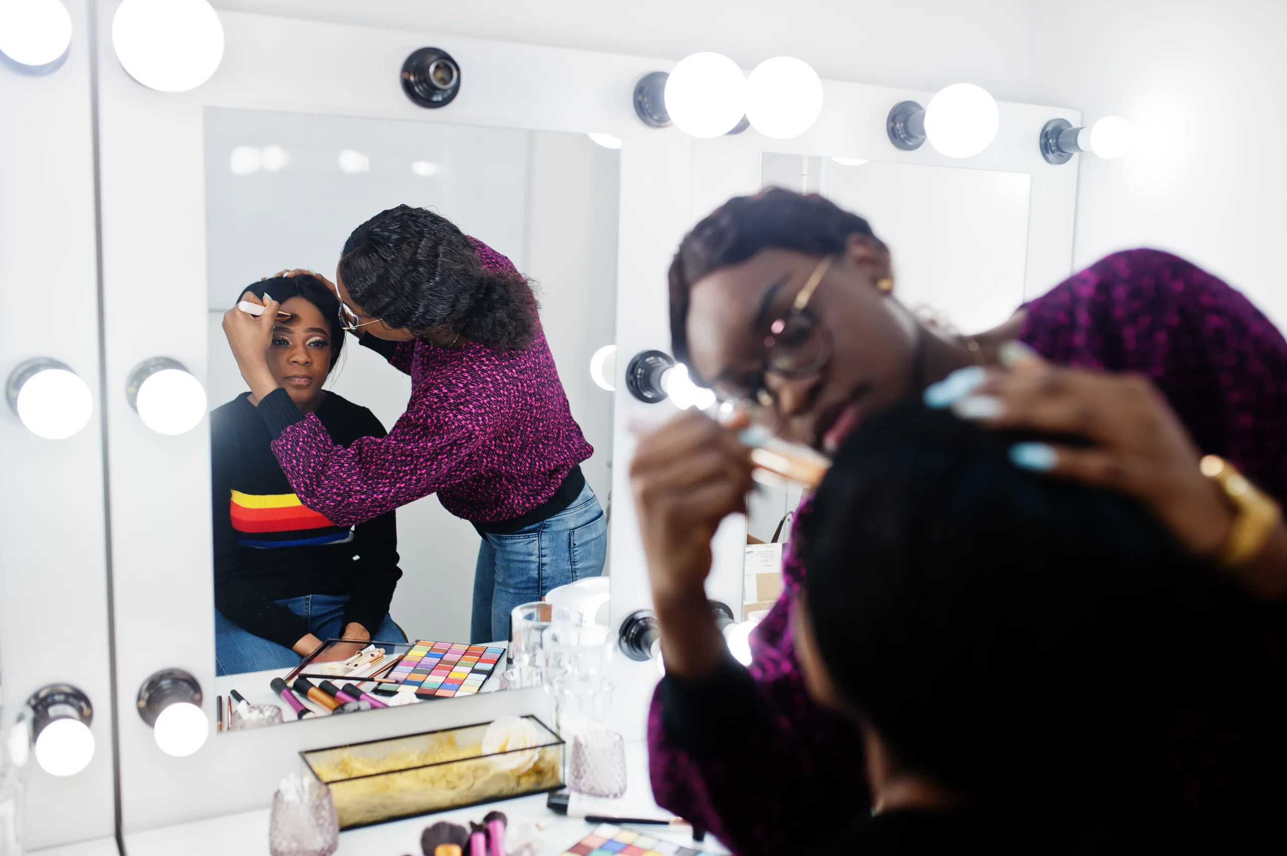 African American woman applying make-up by make-up artist at beauty saloon.